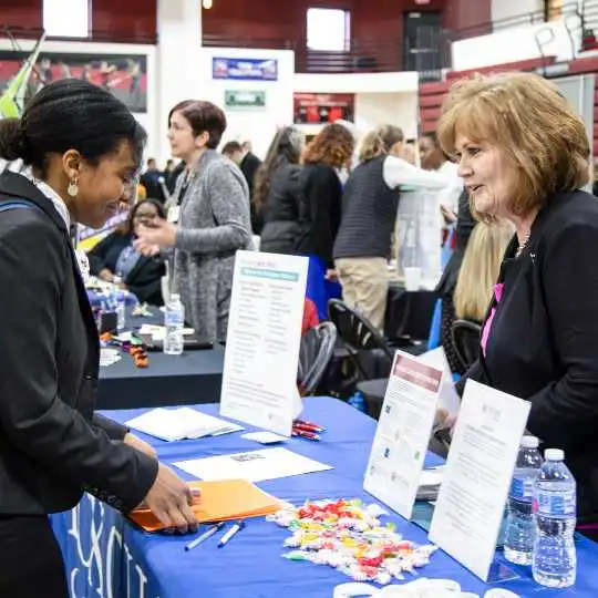 Career fair student and demonstrator lean over a table together.