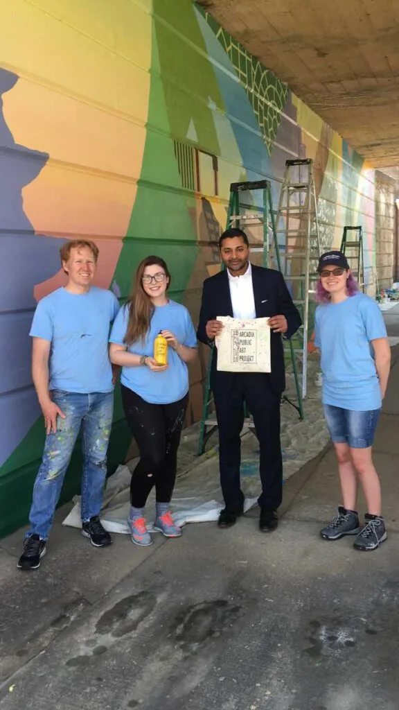 Four people standing in front of mural and smiling at the camera for the Arcadia Public Art Project