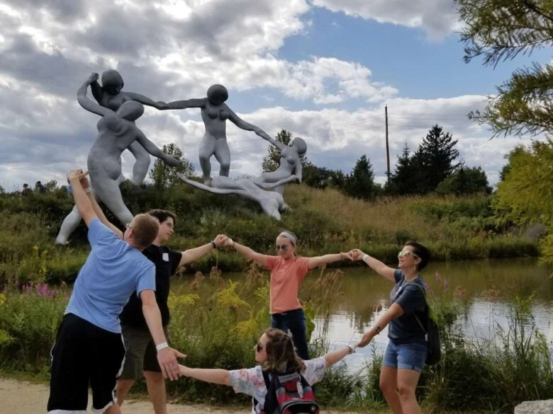 Five students mimic sculpture in background by holding hands and dancing in a circle.