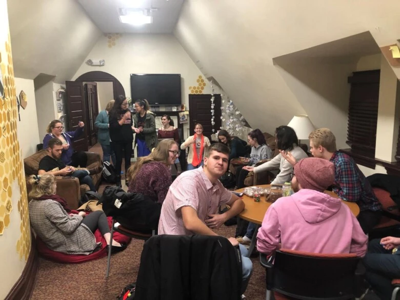 Honors students sit and talk in a small room filled with chairs, tables, and beehive decorations.
