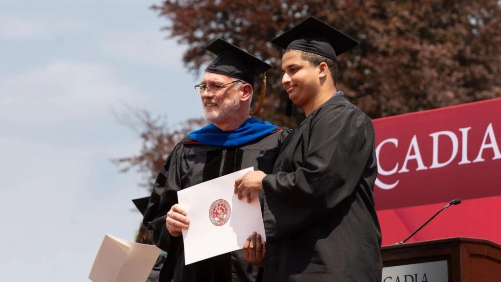 Student poses while receiving diploma at commencement.