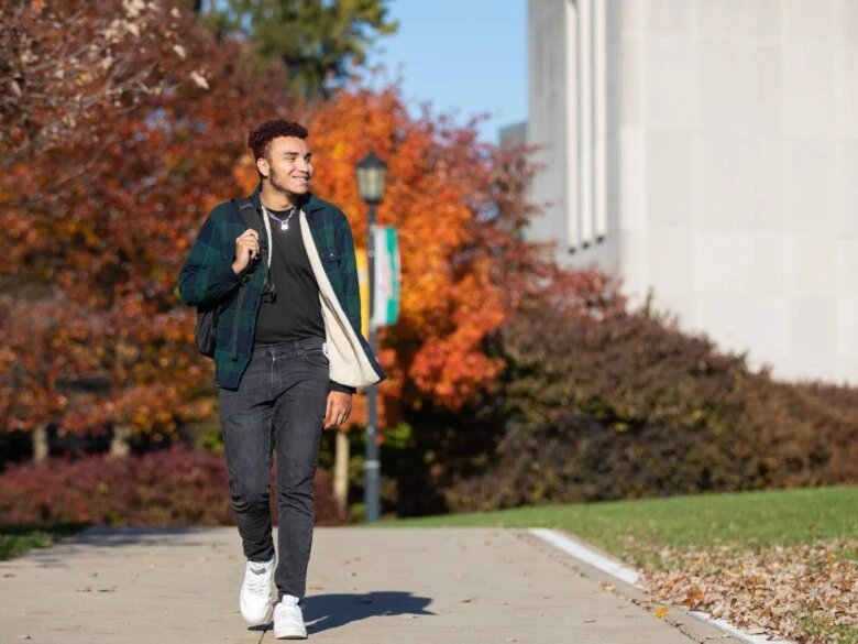 A student smiling and walking outside on campus on a fall day.