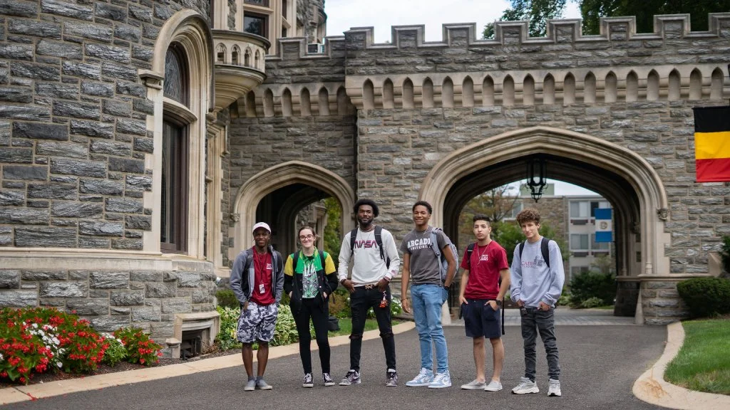 Six students stand together outside on campus while smiling at the camera.