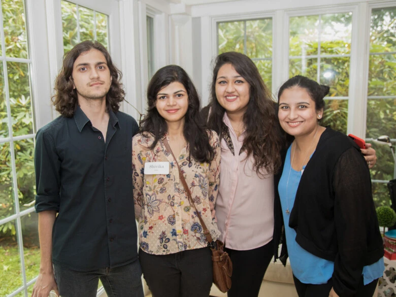 Four international students smiling at the camera while standing in a garden room.