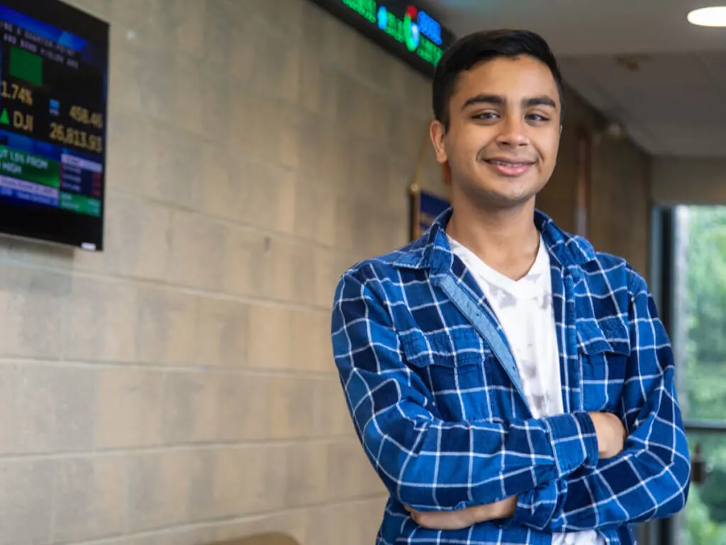 A business student stands in front of a stock ticker.