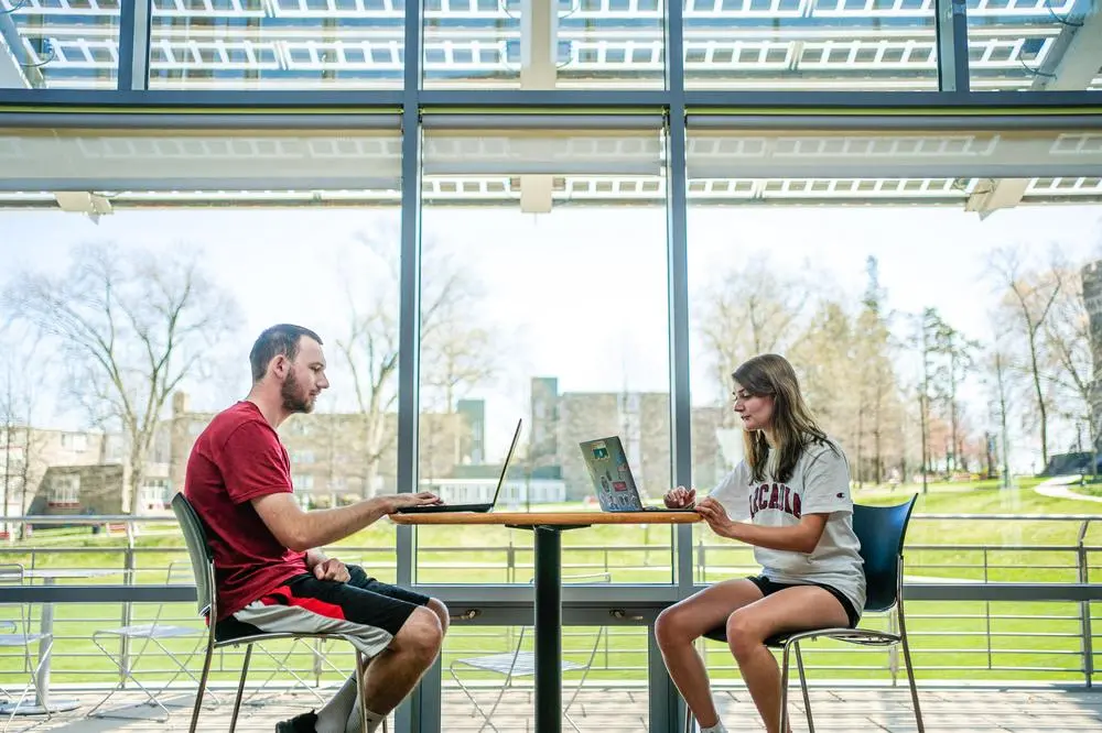 A man student and woman student studying on their laptops in The Chat