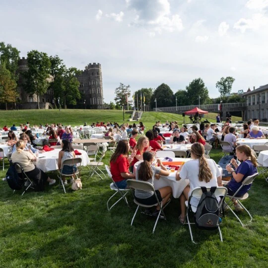 Students sit around tables outdoors and enjoy the Welcome Back Picnic