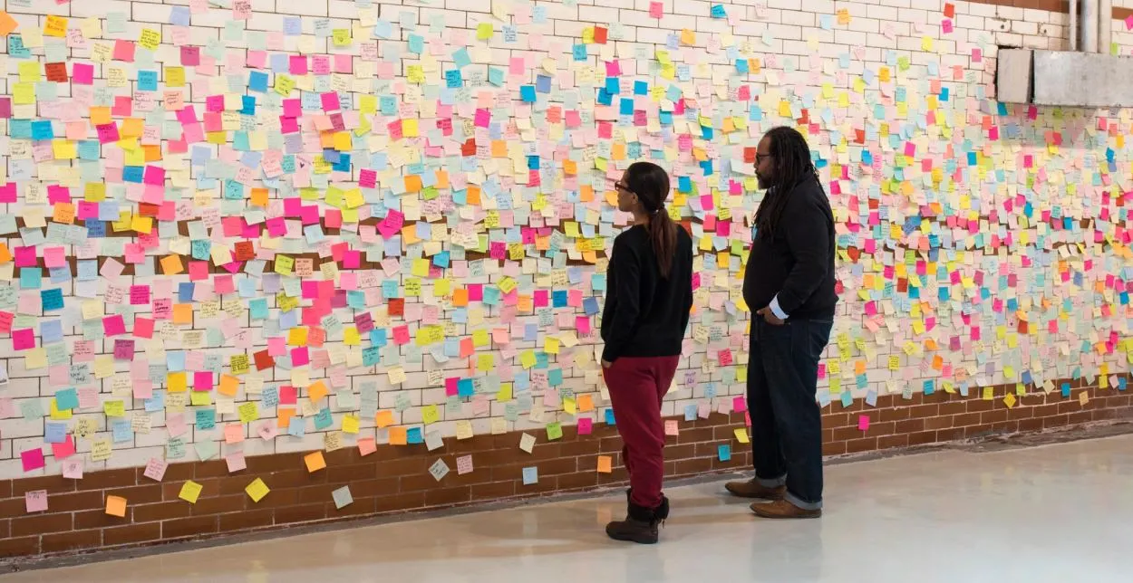 Two people staring at a wall covered in sticky notes