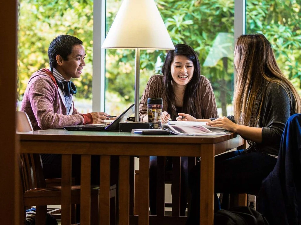 Three students smiling and sitting at a table and working at the Landman Library.