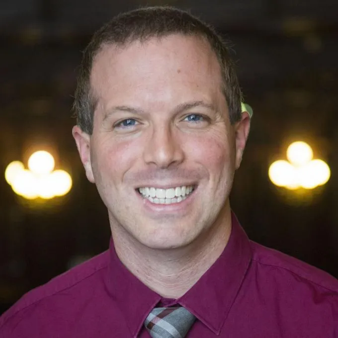 Matthew Heitzman smiles with lights in the background.