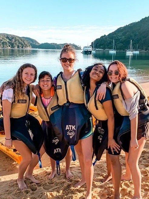 Arcadia student, Jordan Bonnell poses in the center of a group of students on a sunny beach overseas.