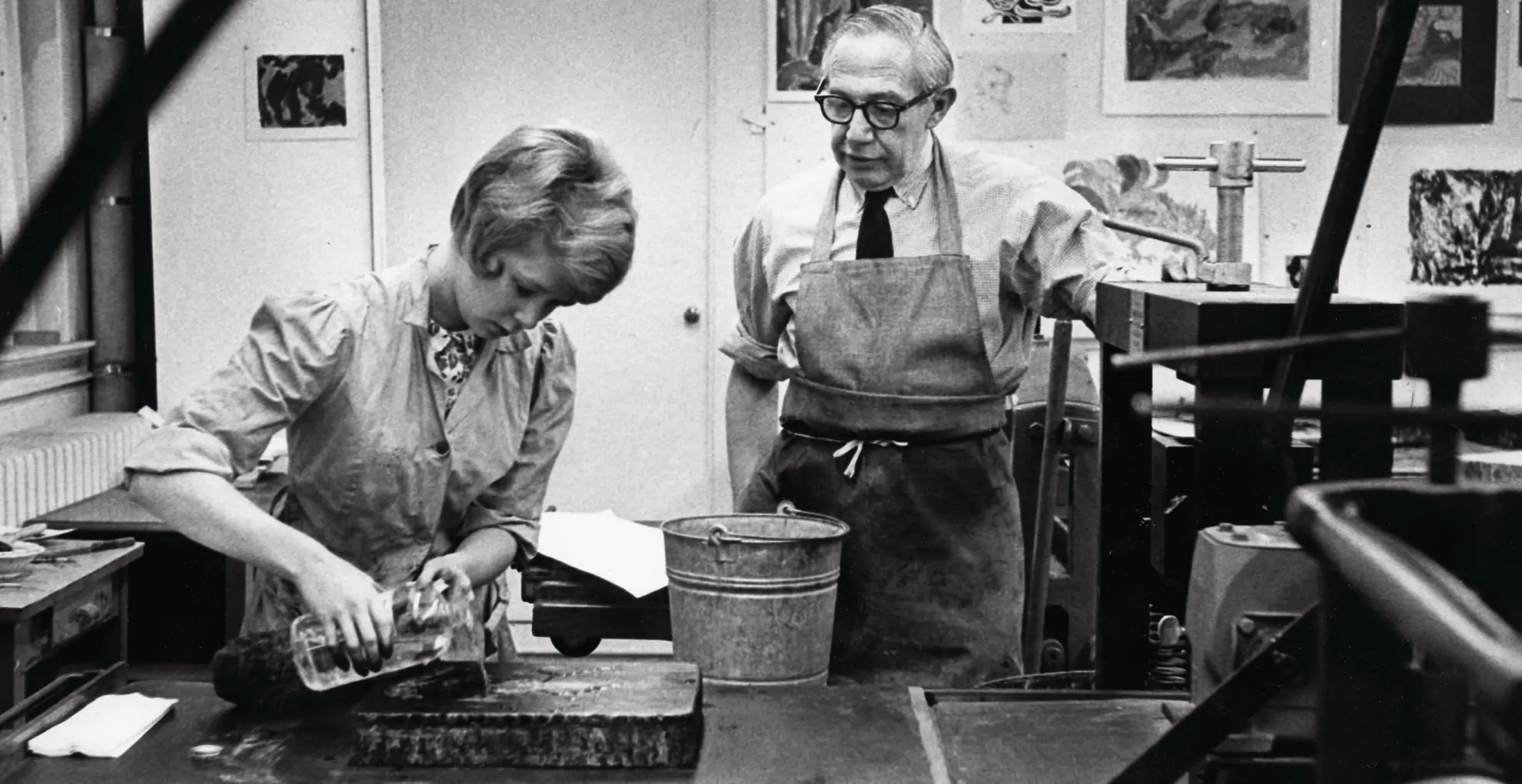A professor guiding a student on pouring liquid for an art project