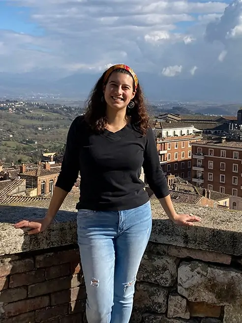 Arcadia student, Alexandra Monge smiles and poses in front of an old city landscape view of Umbra, Italy.