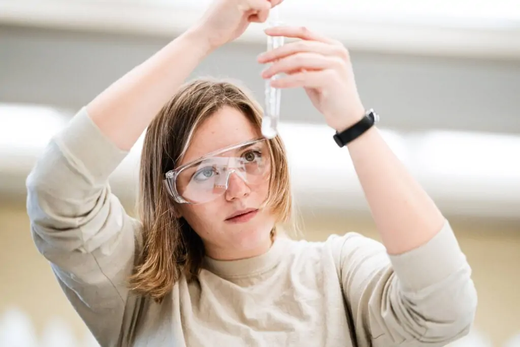 A chemistry student wearing goggles measures solution in a tube vial