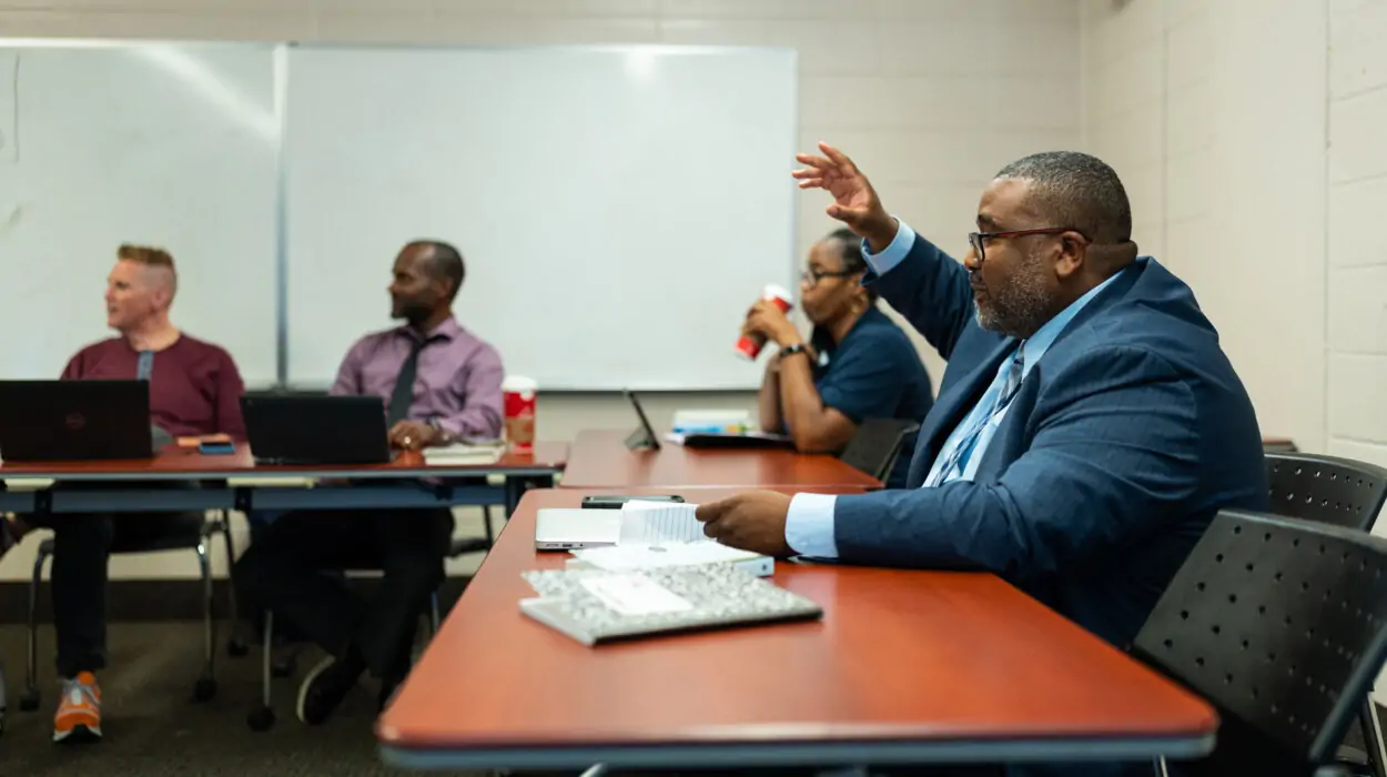 A student in a suit and tie raises his hand in a doctorate level education class.