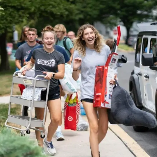 Students carry their belongings from cars on move-in day