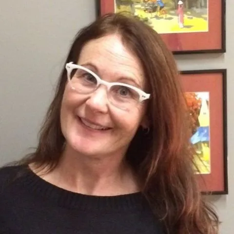 Theresa Barry, wearing glasses, smiles at the camera with head tilted to the side