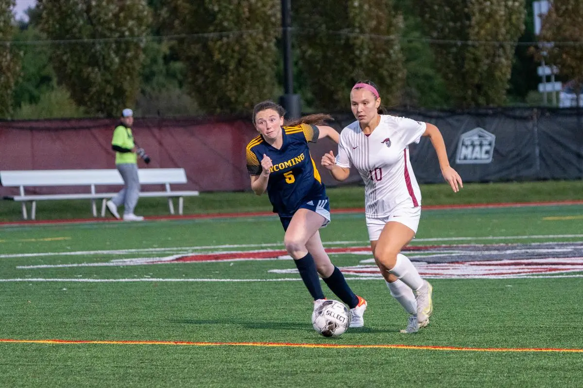 A soccer player on the women's soccer team chases the ball next to a player from Lycoming