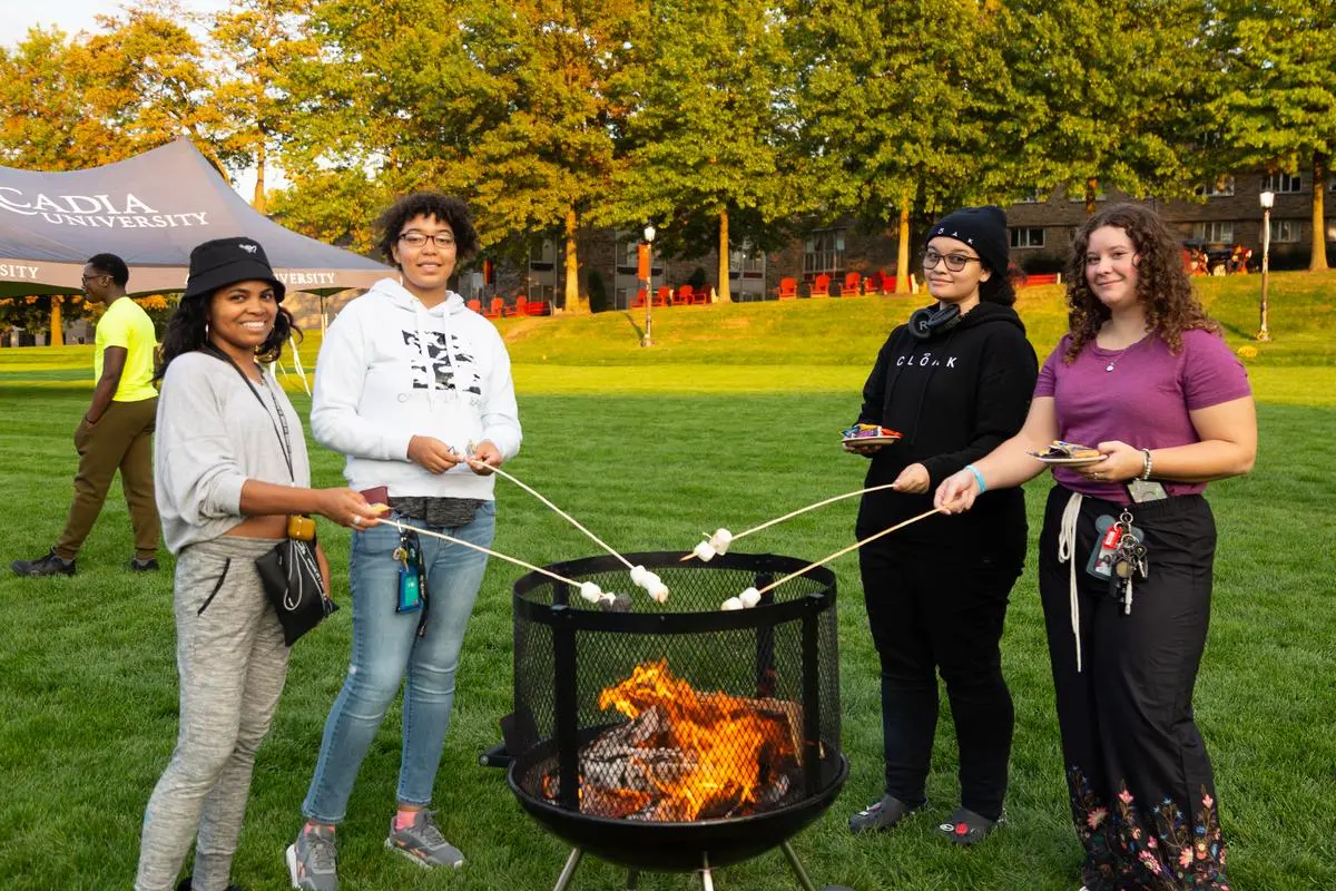 Four students roast marshmallows over a fire pit during homecoming & family weekend 