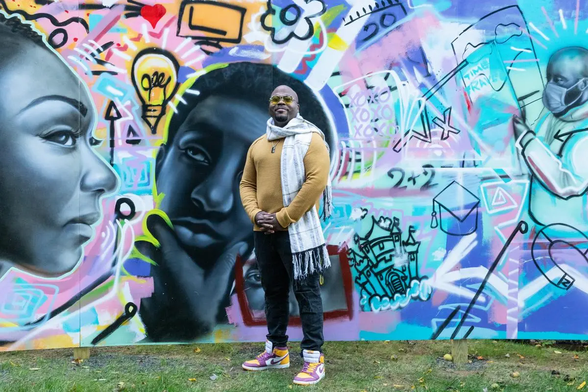 Amir Campbell stands in front of his mural for a photo