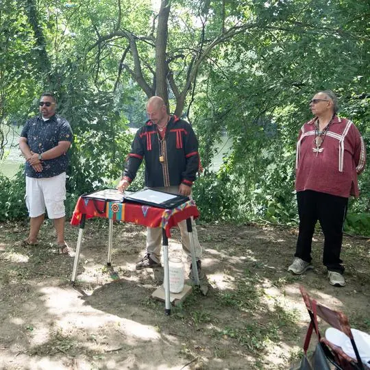 Three people stand outside in an honorary ceremony for the Lenape people