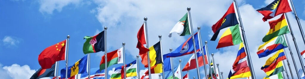 Brightly colored flags from around the globe flap in the wind against a blue sky.