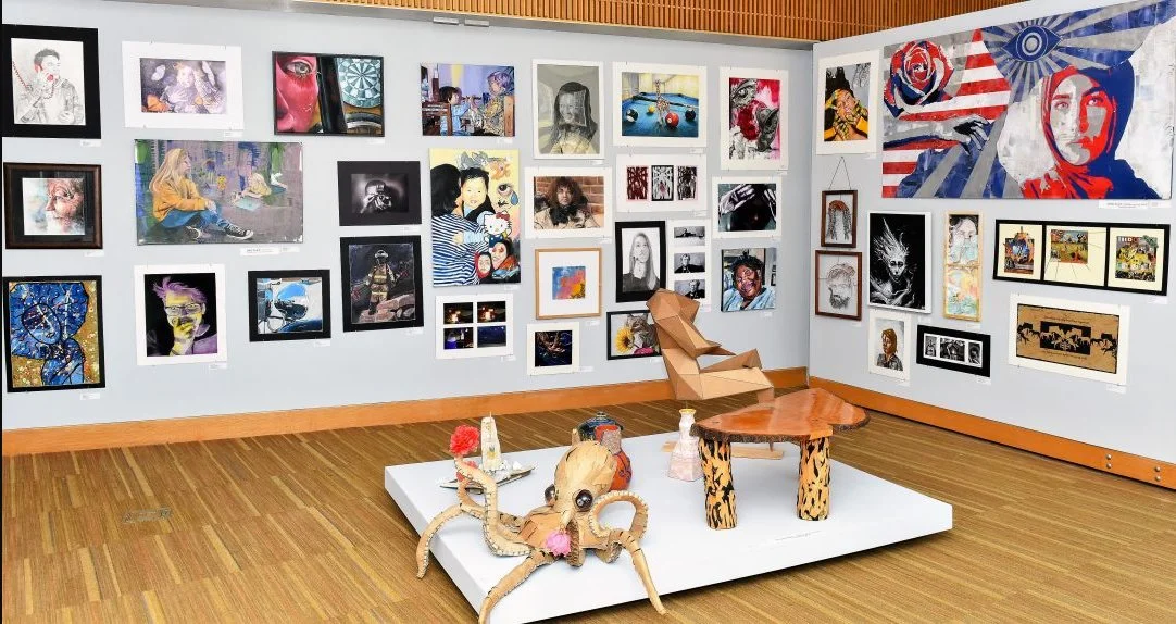 Photo of approximately 15 art pieces in the exhibition on the gallery wall