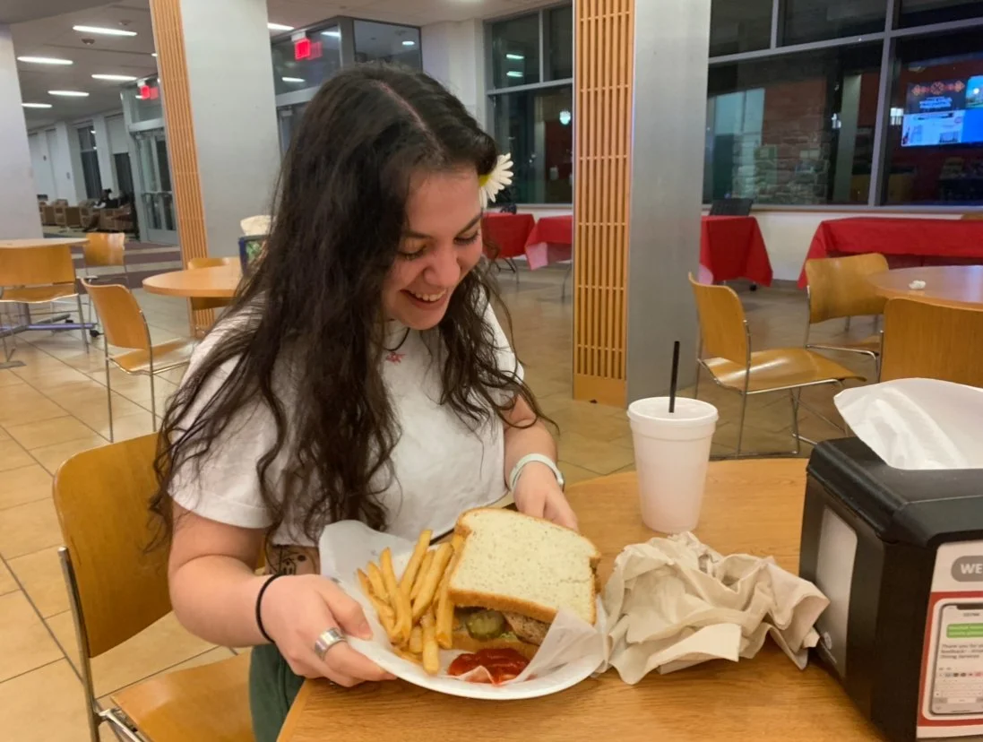 A student smiling while looking at her sandwich and french fries