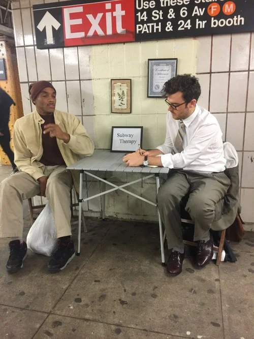 two men sitting at a table with a sign that reads subway therapy