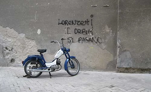 a photo of a motorbike in front of a concrete wall with graffiti