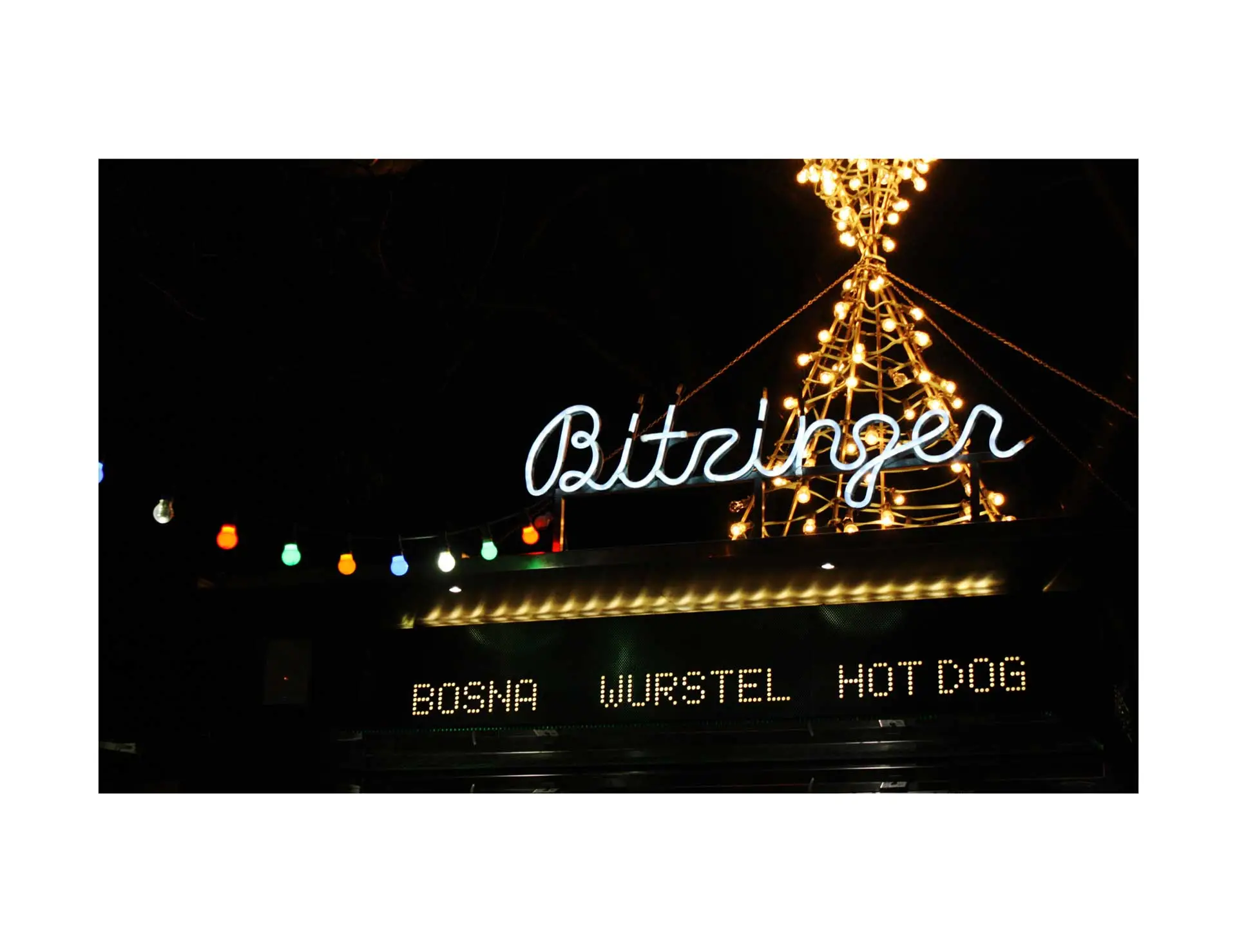 a neon sign that reads "bitzinger" and below it a smaller sign with the words bosna, wurstel, and hot dog