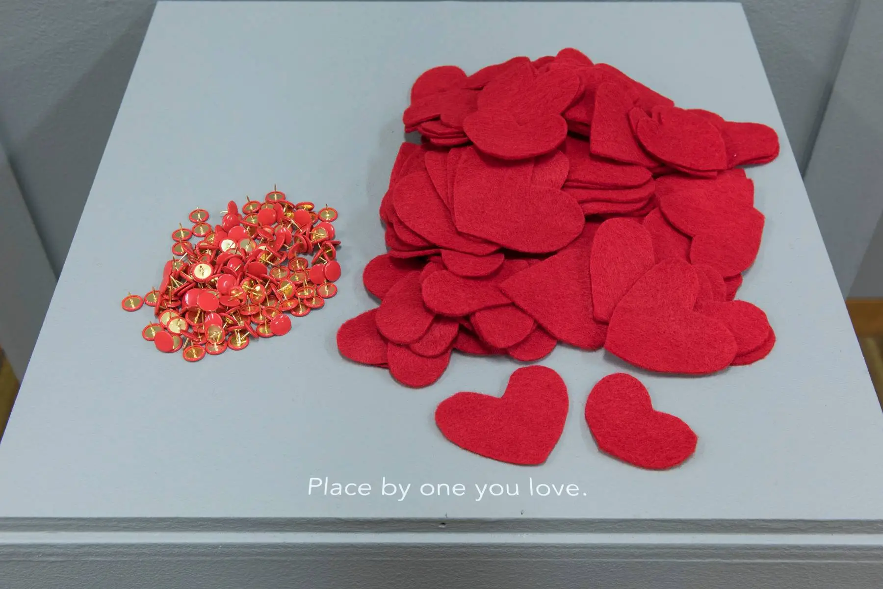 red felt hearts and pins on a pedestal labelled "place by one you love"