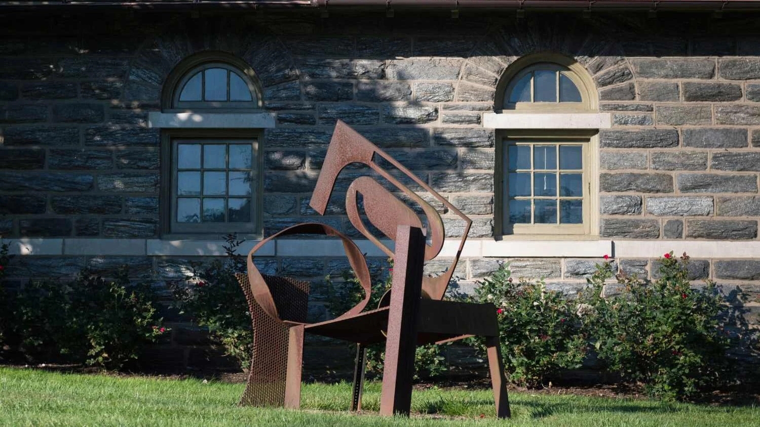a metal sculpture composed of various geometric shapes in front of a stone building