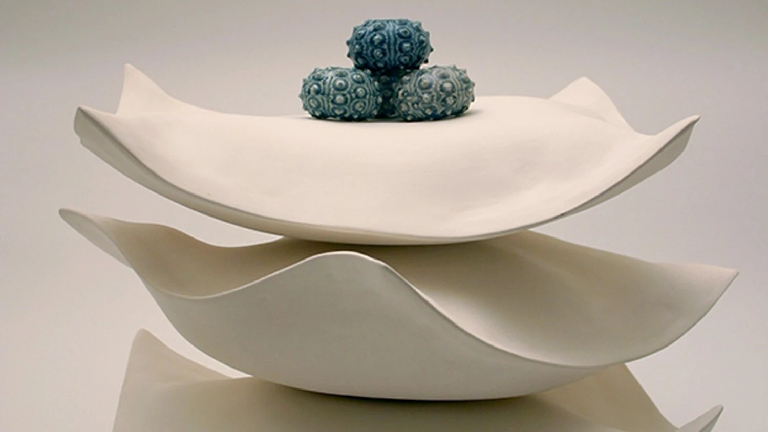 detail of an artwork comprised of three organic shaped ceramic objects stacked on top of each other with four ceramic sea urchins in a group on top
