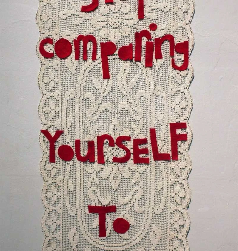 a large vintage doily with the words stop comparing yourself to others in red felt letters