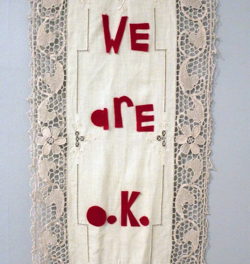 a large vintage cloth embellished with the words we are o.k. in red felt letters