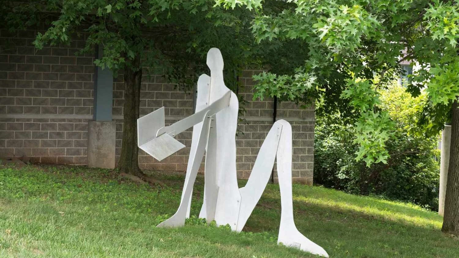 a white metal sculpture that resembles a person reading a book