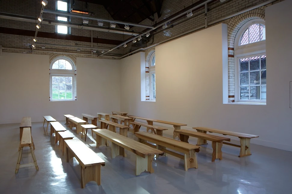 installation view of three rows of handcrafted wooden benches in Spruance Gallery