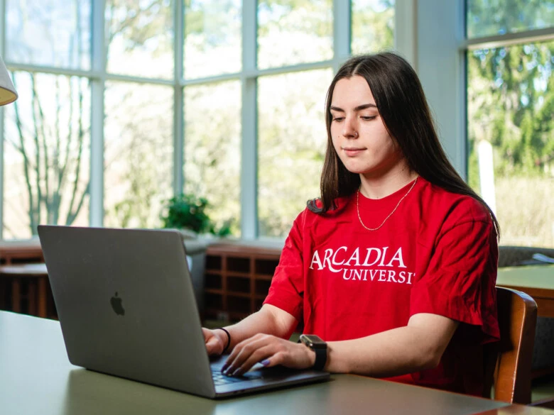 A student wearing a red shirt types into a laptop