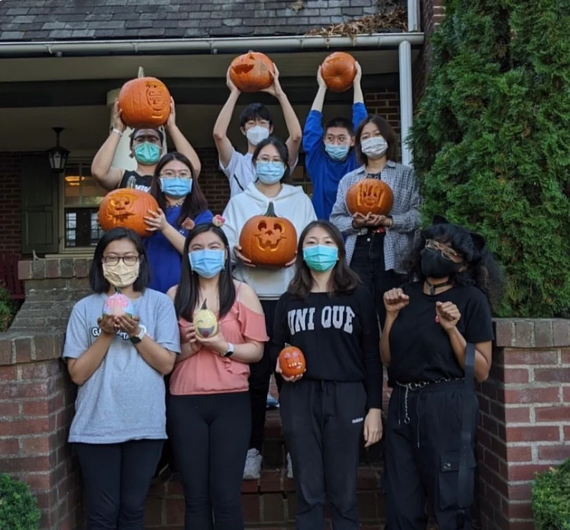 Ten students in a group wearing medical masks and holding jack o lanterns