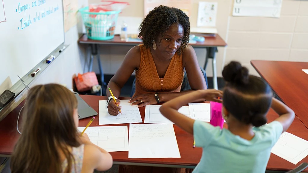 A teacher in the ACLC program instructs two elementary school students in a classroom.