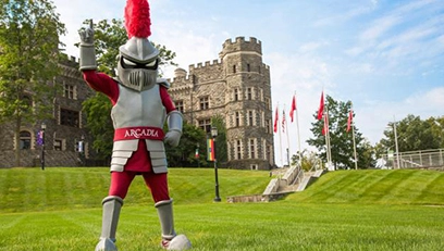 Archie the Arcadia Knight stands on a green lawn in front of the university castle.