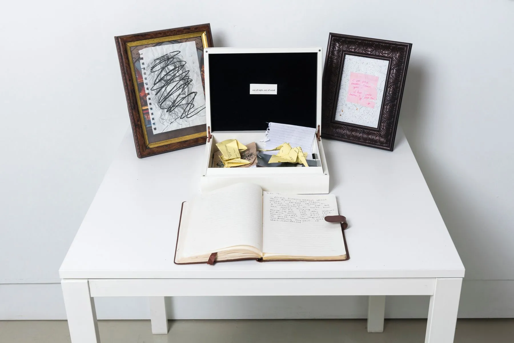 A white table displaying a notebook, a white box filled with paper, and two picture frames
