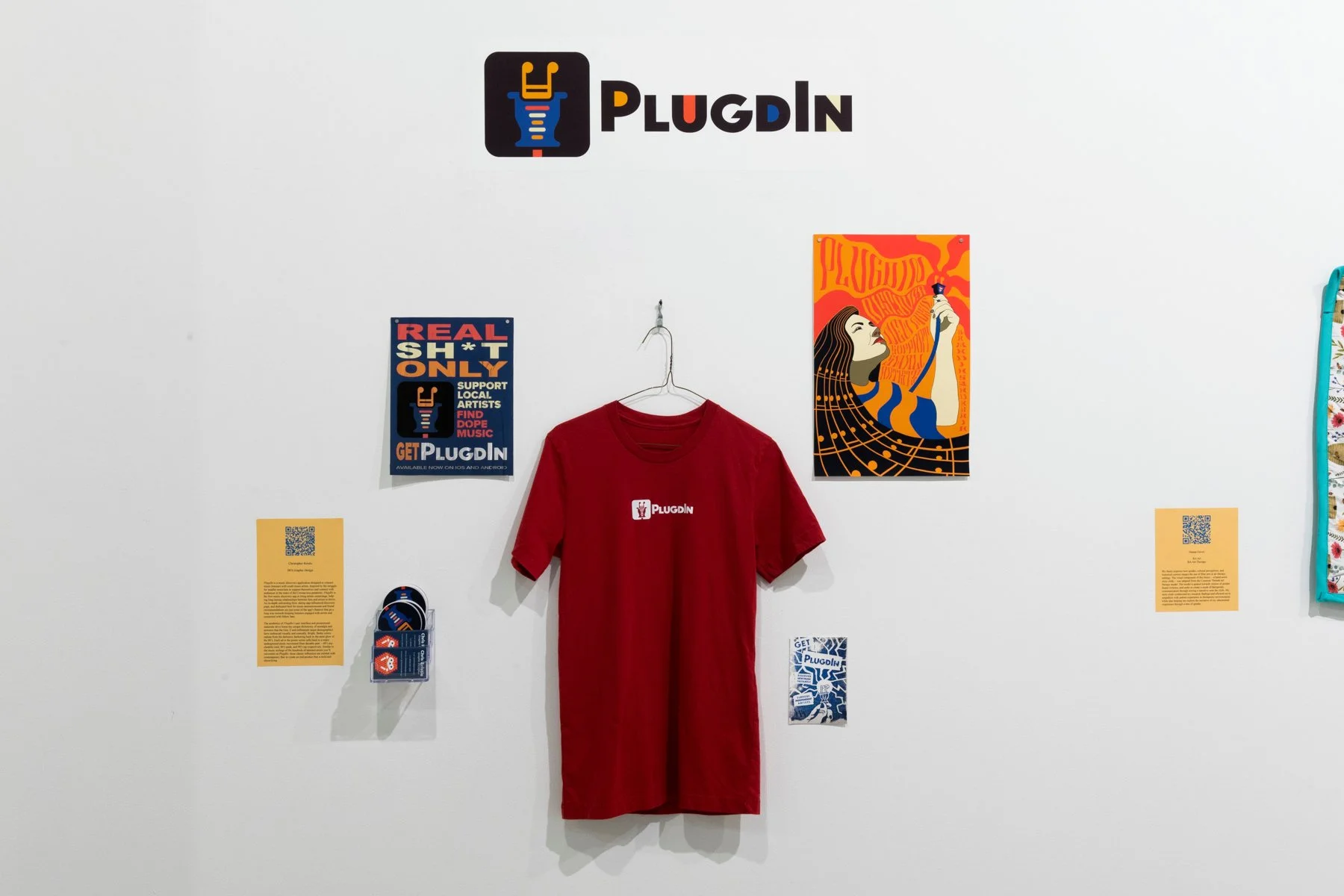 A white wall exhibiting the brand "PLUGIN" with related merchandise and posters