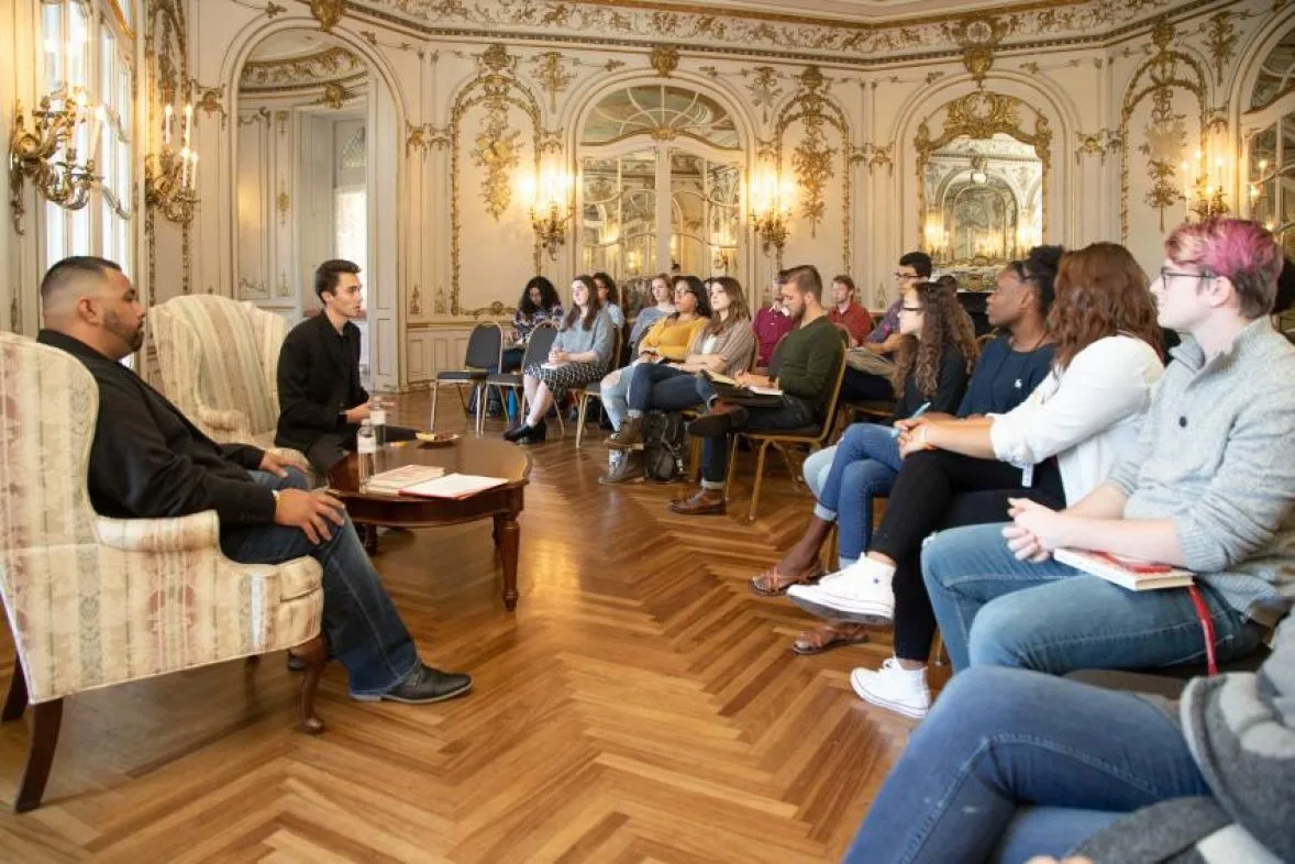 A formal presentation in a gilded room in the Castle filled with students.
