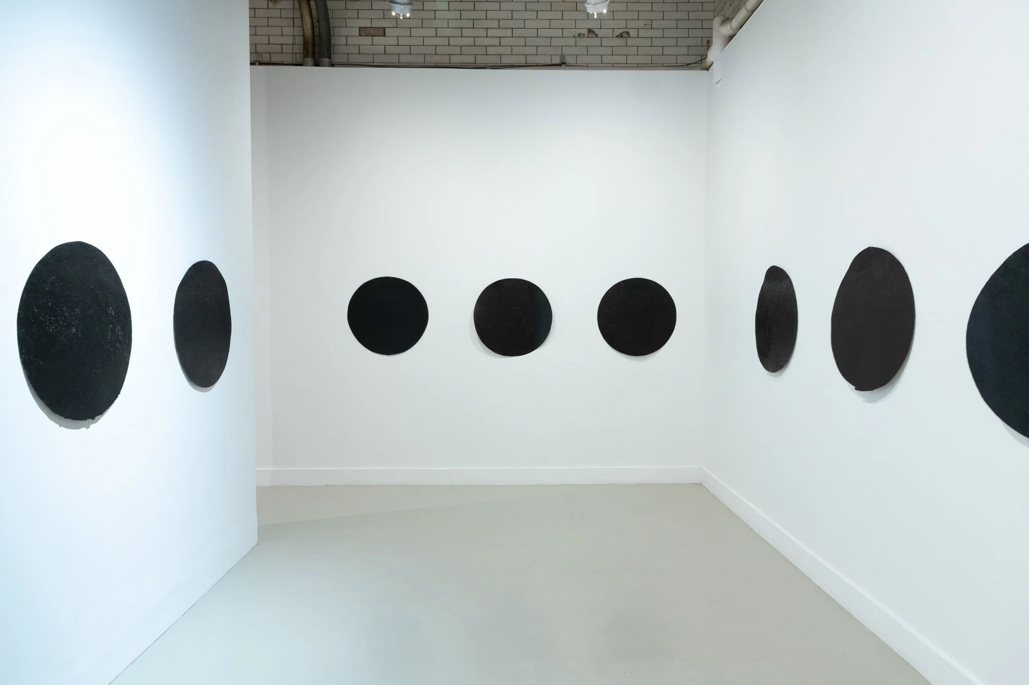 Eight black circle paintings displayed in a white gallery