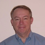 The headshot of a man in a blue collar shirt.