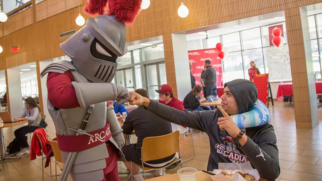Archie the Knight give a student a fist bump in the cafe on campus.