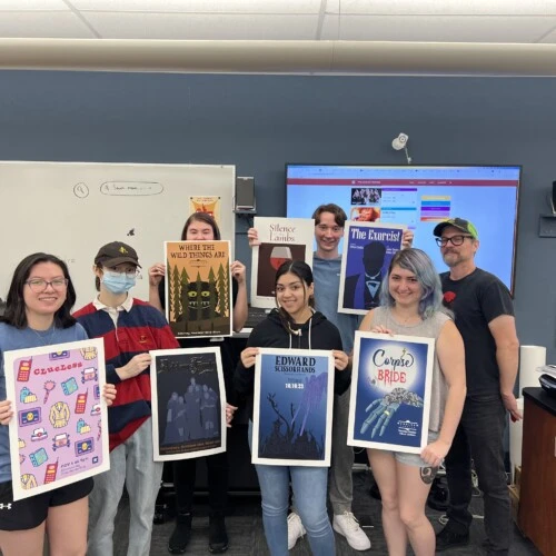 Students holding up posters of their redesigned drawings