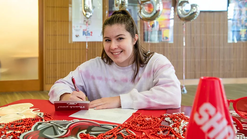 An Arcadia undergraduate student signs a Thank You card at an event table.